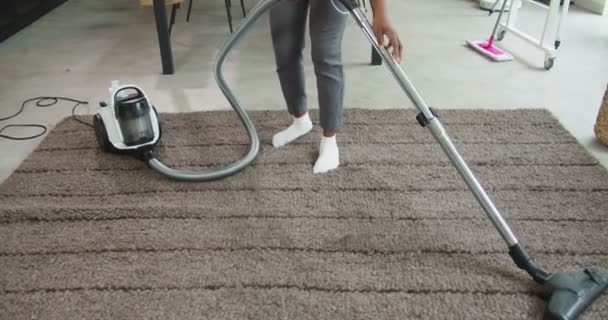 African american woman listening music in headphones and dancing while using vacuum cleaner on carpet at home in the living room during weekend clean. Concept of housekeeping, cleaning house. — Stock Video
