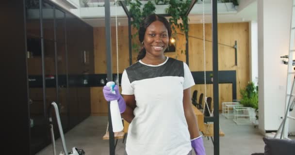 Close up de mulher americana africana alegre segurando spray mais limpo com as mãos em luvas e olhando para a câmera sorrindo. Conceito de limpeza, casa de limpeza familiar, estilo de vida. — Vídeo de Stock