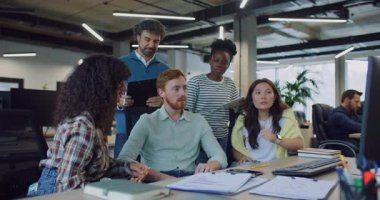 Çoklu etnik gruptan iş arkadaşları kodlarında ya da evraklarında hata arıyorlar. Monitörün önünde oturuyor. İçinde veri olan defterler tutuluyor. Çözüm arıyorum. Arka planda çalışan diğer insanlar.