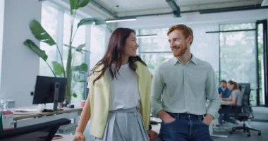 İki insan yan yana duruyor ve güvenle kameraya bakıyor. Siyah saçlı, sarı kazaklı, omuzlarının üzerinde gülümseyen bir kadın. Kollarını kavuşturan kızıl saçlı yakışıklı bir adam.