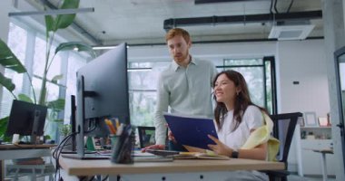 Akıllı lider kadının arkasında duruyor ve bilgisayar işinde ona yardım ediyor. Güzel bir kadın masada oturuyor ve elinde belgelerle klasörü tutuyor. Adam dişiye baş parmak gösteriyor. Üretken takım çalışması.