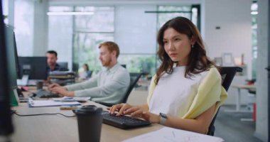 Profesyonel işçi, beyaz iş ofisindeki iş arkadaşının yanında oturuyor. Metni girerken klavyede tuşlara basan güzel bir kadın. Arka planda bilgisayarlar üzerinde çalışan meşgul yöneticiler.