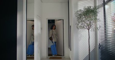 Çekici beyaz kız tatilden eve dönüyor. Girişte mavi bavulu tekerleklerin üzerinde bırakarak. Kapatıyorum. Daha sonra cep telefonunu cebinden çıkardı. İleti giriyor veya yazılıyor.