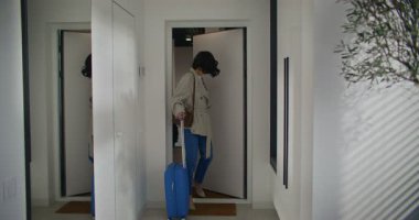 Çekici beyaz kadın seyahatten eve dönüyor. Kapıya mavi bavul bırakmış. Ceketimi çıkarıyorum. Giysileri dolaba yerleştiriyorum. Aynaya bakıyorum. Eve giriliyor.