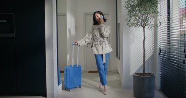 Akıllı telefondan konuşan beyaz, tatlı bir kadın. Evin girişinin yanında duruyor. Genişletilebilir bavul sapına yaslanarak. Ayrılmadan önce akıllı telefondan konuşmak. Sonbahar kıyafeti. İletişim konsepti.
