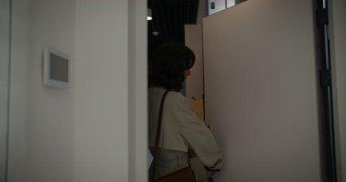 Kamera koridorda kayıyor. Beyaz, kıvırcık siyah saçlı bir kadın daireye giriyor. Market poşeti taşıyorum. Alışverişten eve döndüm. Akıllı telefonunu kullanıyordu. Haberleri kontrol et ya da ağla.