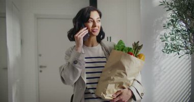 Elinde bir torba dolusu taze yiyecek tutarken, fuayenin ortasında duran beyaz bir kız. Birisiyle aktif olarak cep telefonunda konuşmak. Uzaktan iletişim için akıllı telefon kullanılıyor.