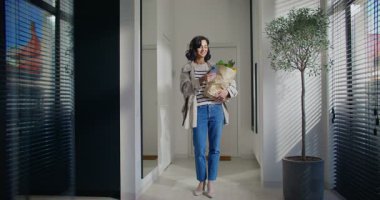 Kafkasyalı esmer, lobinin ortasında duruyor. Tek eliyle bir torba erzak tutuyor. Kot pantolon, şık bir ceket ve yüksek topuklu ayakkabı giyiyor. Mobil cihaz kullanılıyor. Kocaya ya da sevgiliye mesaj yazılıyor.