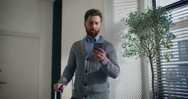 Kamera yakışıklı beyaz bir erkeğin etrafında hareket ediyor. Sakallı ve iş kıyafetli bir adam dairenin ortasında duruyor. Tek elle bavulu tutuyor. Akıllı telefon kullanıyor. İleti gönderiliyor.