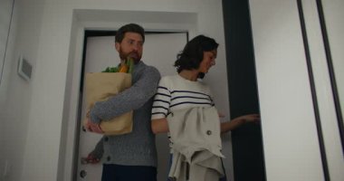 Beyaz bir çiftin alışveriş dönüşü çekilmiş kamera görüntüsü. Kadın çantasını ve yağmurluğunu dolaba bırakmış. Yemek hazırlamak için yan odaya yemek getiriyorum. Malzemeler alınıyor.