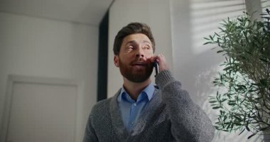 Kamera, sakallı beyaz erkekten yavaşça uzaklaşıyor. Akıllı telefonla konuşurken uzun bir fuayenin ortasında duran bir adam. Uzaktan iletişim konsepti. Taksi bekliyorum. Paketlenmiş çanta.