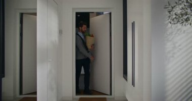 Sakallı, yakışıklı, beyaz bir erkek işten sonra eve geliyor. İşten çıktıktan sonra alışveriş yapmak. Apartmana dönmeden önce alışverişe gidiyorum. Mutlu adam yemek yapmaya hazırlanıyor. Sevinçle gülümsüyor.