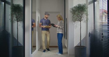 Modern teslimat konsepti. Kurye, kadına çevrimiçi mağazadan talep edilen ürünü sağlıyor. Uzaktan satın alma. Kadın, imzasını atıyor. Memnun bir müşteri. Paketleri açmaya gidiyorum..