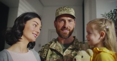 Kafkasyalı mutlu bir ailenin yakın görüntüsü. İnsanlar gülümserken birbirlerine bakarlar. Askeri üniformalı sakallı adam. Baba karısına ve kızına sarılıyor. Gülümserken doğrudan kameraya bakıyorum..