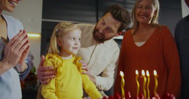 Kafkasyalı küçük bir kızın doğum günü pastasına mum üflerken yakın görüntüsü. Aile toplanıyor evlat. Herkes alkışlıyor ve alkışlıyor. Küçük kız mutluluktan gülümsüyor.