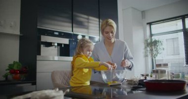 Kafkasyalı bir annenin küçük kızıyla oyun oynaması. Yiyecek bir şeyler hazırlıyorum. Küçük çocuk mutfakta yardımcı olmaya çalışıyor. Malzemeleri karıştırmak için büyük cam kase kullanılıyor..