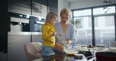 Karıştırma kabına un döken kaşık kaşık beyaz bir kız. Şefkatli bir anne, küçük kızını mutfakta pişirmeyi öğretiyor. İnsanlar diğer aile üyeleri için lezzetli yemekler hazırlıyorlar..