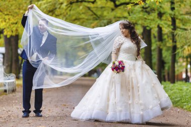 Yeni evliler parkta yürürler ve bir fotoğrafçıya poz verirler.