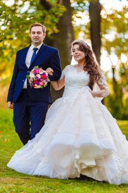 Yeni evliler parkta yürürler ve bir fotoğrafçıya poz verirler.