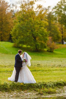 Yeni evliler parkta yürürler ve bir fotoğrafçıya poz verirler.