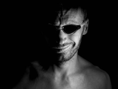 Tıraşsız yetişkin beyaz adam gözlük yüzme portresi. O manyak gibi gülümser ve delilik ya da deli gibi görünüyor. Siyah ve beyaz çekim, düşük anahtar aydınlatma. Siyah izole.