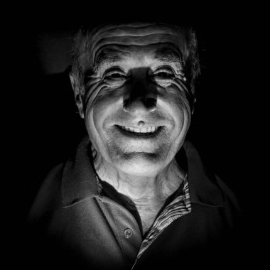 Gülümseyen yaşlı beyaz bir adamın portresi. Siyah beyaz çekim, düşük tuşlu ışıklandırma. Siyah üzerinde izole.