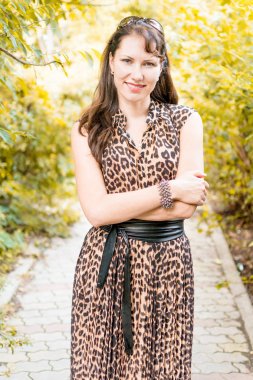 Yazlık parkın ara sokağında güzel elbiseli mutlu ve çekici genç beyaz bir kadın portresi. Güzel doğal sarı arka plan.