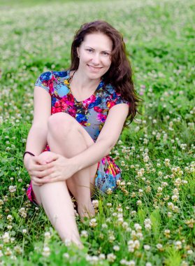 Yaz parkında yonca çiçekleri ile çim üzerinde güzel elbiseli mutlu ve çekici genç beyaz kadın yumuşak portre.