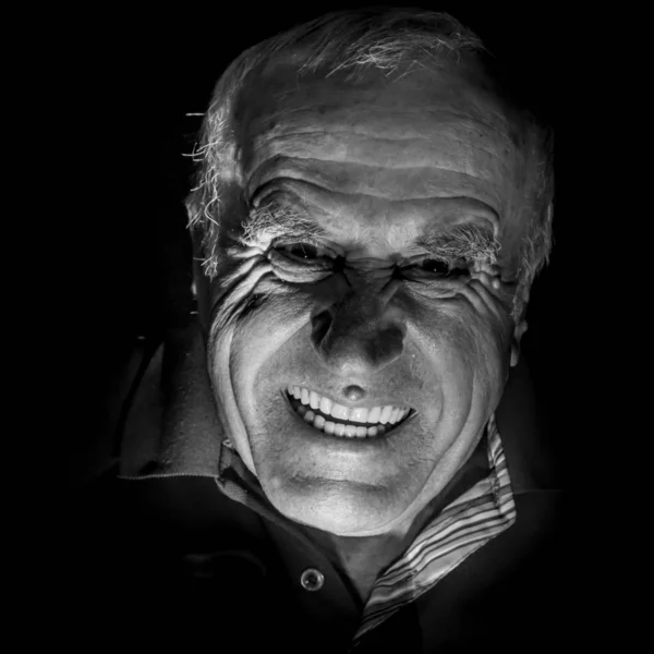 Portrait of old caucasian man who scares watcher. Fear and scare concept. Black and white shot, low-key lighting. Isolated on black.