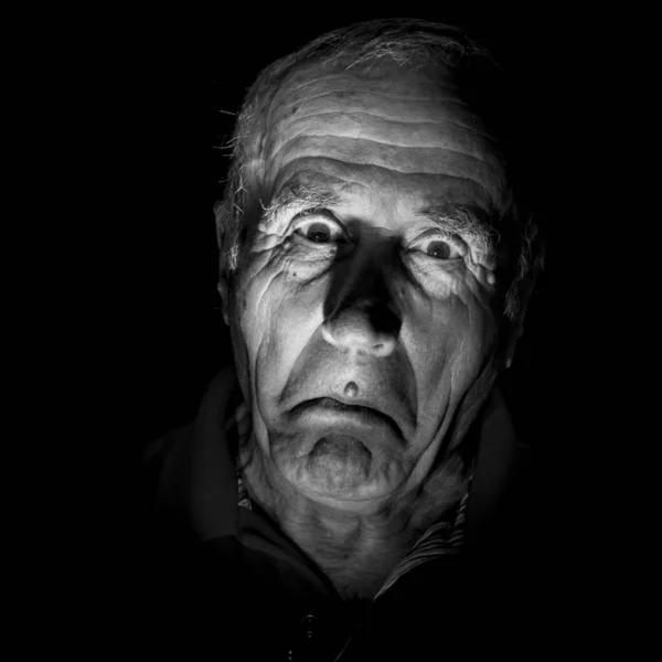 Portrait of old caucasian man with funny expression. Black and white shot, low-key lighting. Isolated on black.