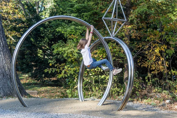 Beyaz kız parkta oynar ve güneşli bir günde metal heykele tırmanır. Aktif spor ve tatiller. Tırmanma eğitimi, sağlıklı yaşam tarzı konsepti.