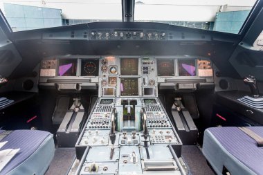 Modern yolcu uçağındaki pilot kabininin iç görüntüsü. Gösterge panelinde bir sürü düğme, navigasyon cihazı var. Havaalanı terminali pencerenin dışında görünüyor. Havacılık ve ulaşım.