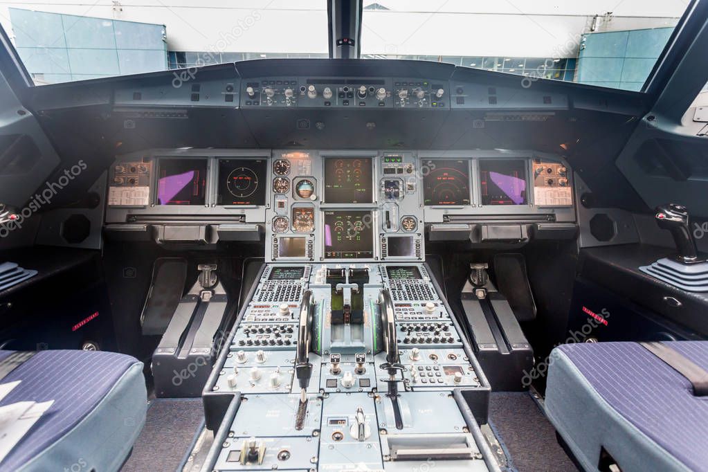 Interior view of pilot cabine in actual modern passenger jet airplane. Many buttons, navigation devices on dashboard. Airport terminal is visible outside the window. Aviation and transportation.