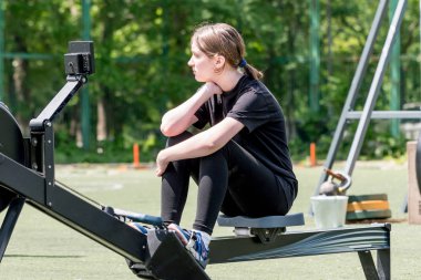 Genç beyaz kız kürek çekme makinesinde oturur ve antrenman için kürek çekme yarışmasına hazırdır. Çocukların spor ve müsabakaları, aktif spor.