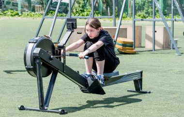 Genç beyaz kız kürek çekme yarışmasında kürek çekme makinesinde fiziksel egzersiz yapıyor. Çocukların spor ve müsabakaları, aktif spor.