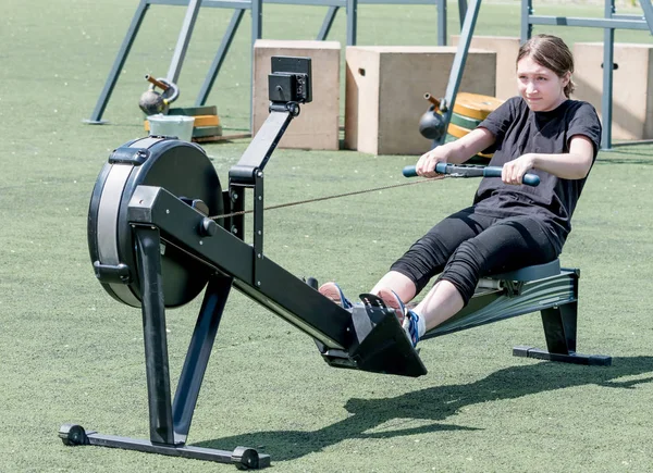 Genç beyaz kız kürek çekme yarışmasında kürek çekme makinesinde fiziksel egzersiz yapıyor. Çocukların spor ve müsabakaları, aktif spor.
