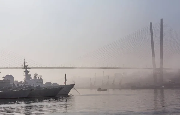 Russia, Vladivostok. View with heavy fog on Golden Horn Bay (or Zolotoy Rog) with Golden Bridge (Zolotoy bridge) and parking of military battleships of Russian Pacific Navy with few battle cruisers.