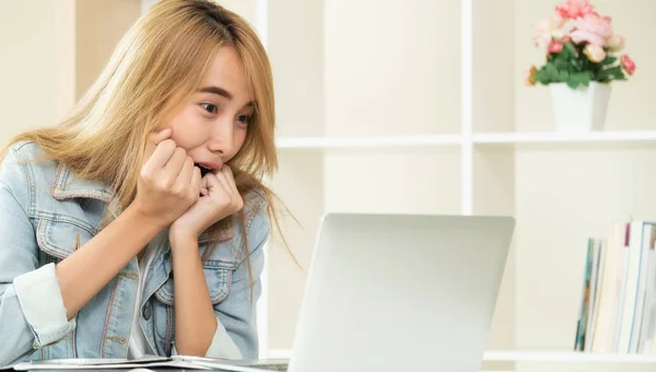 Cute woman feels amazed, excited or surprised while looking at laptop computer in cozy home office. Concept of amazing sale advertising and lucky prize winner.