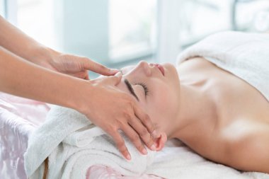 Lüks bir spa merkezinde masaj terapisti tarafından yüz masajı ve spa tedavisi için kaplıcaya uzanmış rahat bir kadın. Sağlık, stres atma ve gençleştirme kavramı.
