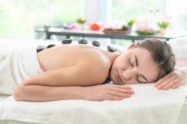 Kadın kaplıca salonunda profesyonel güzellik terapisti tarafından sıcak taş masajı görüyor. Lüks sağlık, sırt stresi ve gençleştirme kavramı..