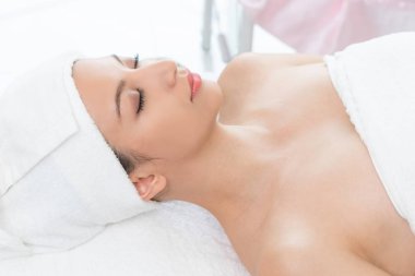 Spa yatağında uzanan rahat genç bir kadın lüks bir spa merkezinde yüz bakımı ve masaj için hazırlandı. Sağlık, stres atma ve gençleştirme kavramı.