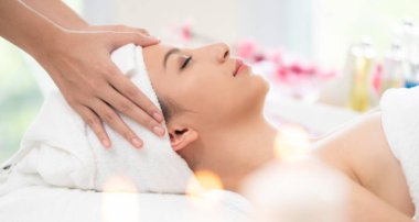 Lüks bir spa merkezinde masaj terapisti tarafından yüz masajı ve spa tedavisi için kaplıcaya uzanmış rahat bir kadın. Sağlık, stres atma ve gençleştirme kavramı.