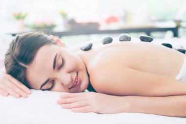 Kadın kaplıca salonunda profesyonel güzellik terapisti tarafından sıcak taş masajı görüyor. Lüks sağlık, sırt stresi ve gençleştirme kavramı..