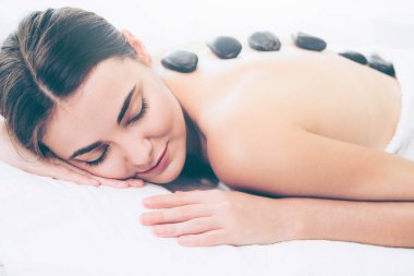 Kadın kaplıca salonunda profesyonel güzellik terapisti tarafından sıcak taş masajı görüyor. Lüks sağlık, sırt stresi ve gençleştirme kavramı..