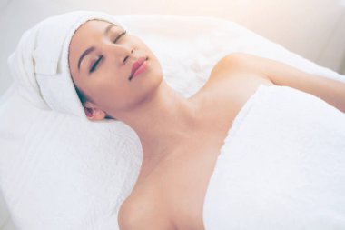 Spa yatağında uzanan rahat genç bir kadın lüks bir spa merkezinde yüz bakımı ve masaj için hazırlandı. Sağlık, stres atma ve gençleştirme kavramı.