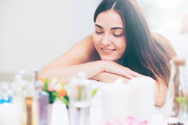 Relaxed woman lying on spa bed for aromatherapy massage in luxury spa with blurred foreground of spa treatment set including aromatic oil, candle and herbal scrub. Wellness and healing concept.