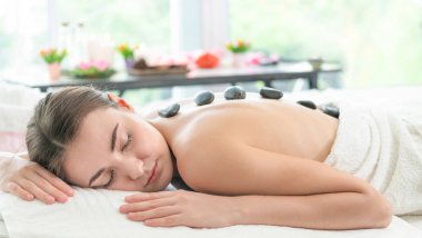 Kadın kaplıca salonunda profesyonel güzellik terapisti tarafından sıcak taş masajı görüyor. Lüks sağlık, sırt stresi ve gençleştirme kavramı..