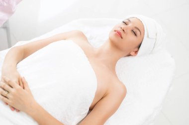 Spa yatağında uzanan rahat genç bir kadın lüks bir spa merkezinde yüz bakımı ve masaj için hazırlandı. Sağlık, stres atma ve gençleştirme kavramı.