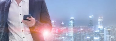 Genç işadamı cep telefonunuzun ve modern şehir binaları arka plan ile. Gelecekteki telekomünikasyon teknolojisi ve internet şeyler (çok) kavramının.