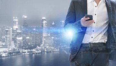 Genç işadamı cep telefonunuzun ve modern şehir binaları arka plan ile. Gelecekteki telekomünikasyon teknolojisi ve internet şeyler (çok) kavramının.